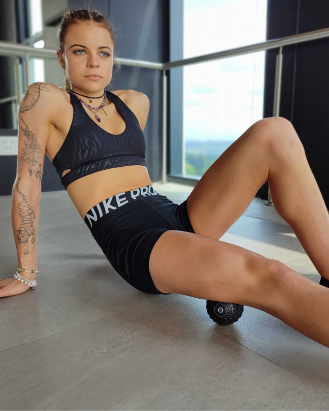 Woman in Nike athletic wear using a foam roller on a tiled floor.